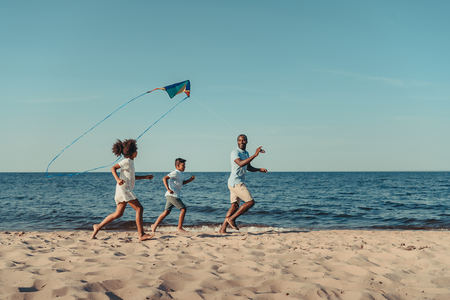 happy african american father and kids playing with kite on beachの写真素材