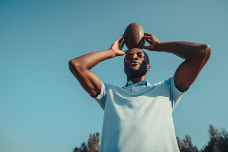 low angle view of african american man holding rugby ball above headの写真素材
