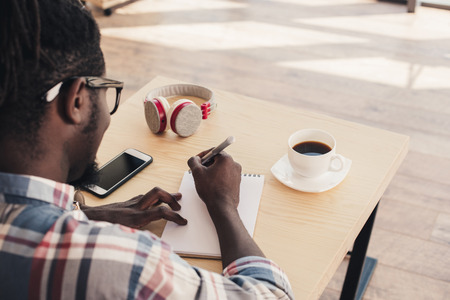 african american man writing in notepad during coffee break in cafeの写真素材