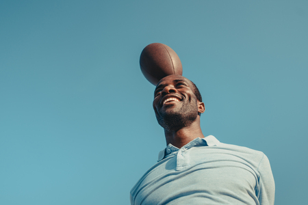 low angle view of smiling african american man with rugby ball above headの写真素材