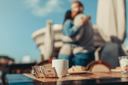cup of coffee and money on table of cafe with blurred embracing couple on backgroundの写真素材