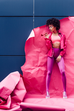 fashionable african american model with horn posing in 80s style clothes with pink paperの写真素材
