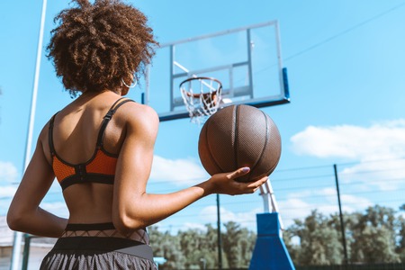young african-american woman in sports bra holding a basketball ball on her hand