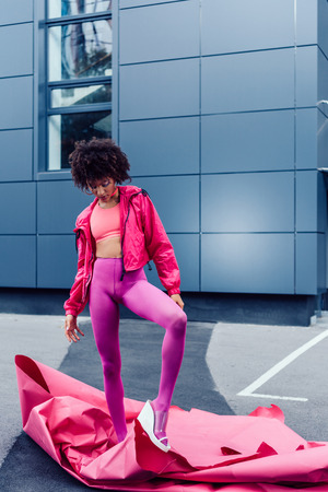 fashionable african american girl posing in 80s style clothes with pink paperの写真素材