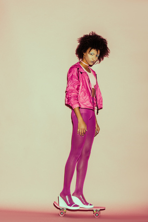 afro 80s girl in pink clothes posing with penny board for fashion shoot