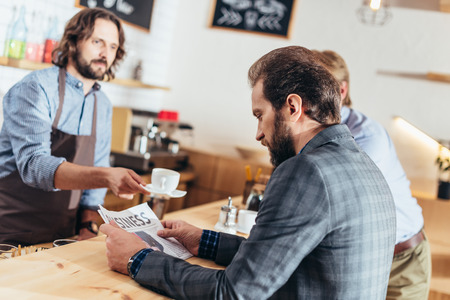 serious bearded middle aged businessman reading newspaper in cafeの写真素材