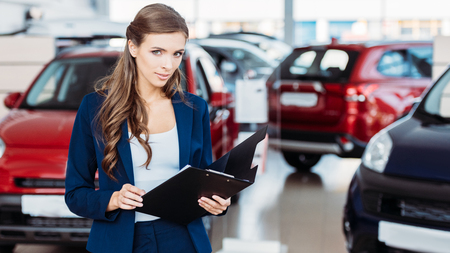 Attractive manager of car showroom standing with clipboard folder and looking at the camera の写真素材