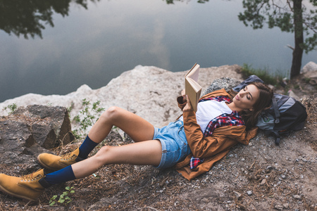 beautiful young woman reading book on nature near lakeの写真素材