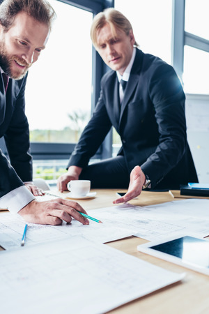 cropped shot of smiling middle aged businessmen working with blueprints in officeの写真素材