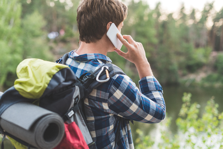 back view of hiker talking by phone outdoors while having tripの写真素材