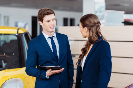 Female and male managers standing and talking about work in a car showroomの写真素材