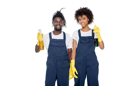 portrait of smiling african american cleaners in rubber gloves with detergents in hands looking at camera isolated on whiteの写真素材