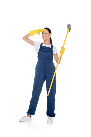 smiling asian cleaner in rubber gloves with broom in hand isolated on white の写真素材