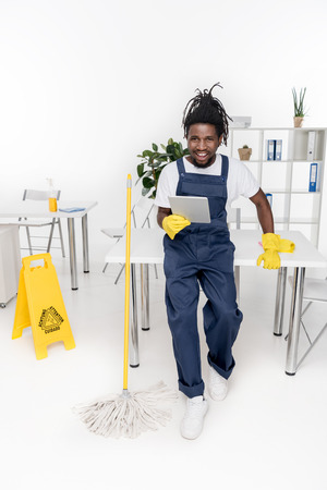 cheerful african american cleaner using digital tablet and smiling at cameraの写真素材