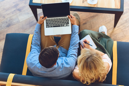 overhead view of couple using laptop and taking notes in cafeの写真素材
