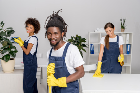multiethnic group of professional cleaners in rubber gloves smiling at camera while working togetherの写真素材