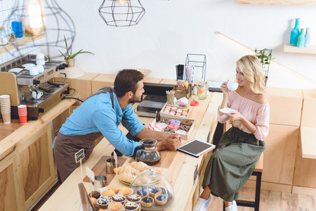high angle view of young barista looking at beautiful woman drinking coffee in cafeの写真素材