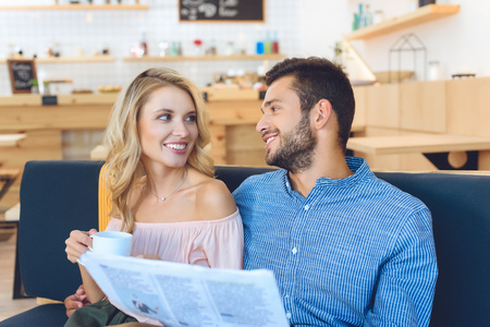 happy young couple with coffee cup and newspaper smiling each other in cafeの写真素材