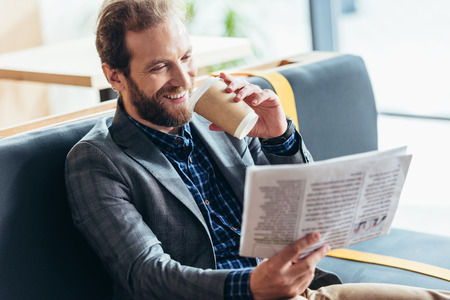 handsome smiling middle aged man reading newspaper and drinking coffee in cafeの写真素材