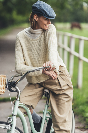 beautiful smiling stylish woman sitting on bike at countrysideの写真素材