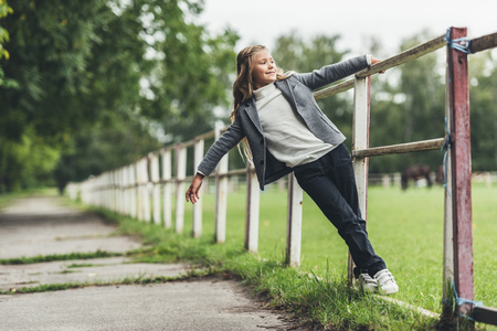 adorable blonde child sitting on fence at countryside の写真素材