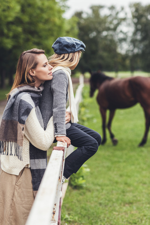 stylish mother and daughter standing at paddock with horseの写真素材