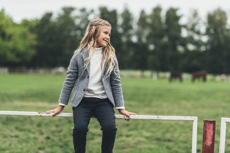 adorable blonde child sitting on fence at countryside の写真素材