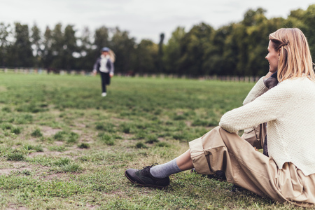 stylish woman in autumn outfit sitting at countryside, her daughter running behindの写真素材