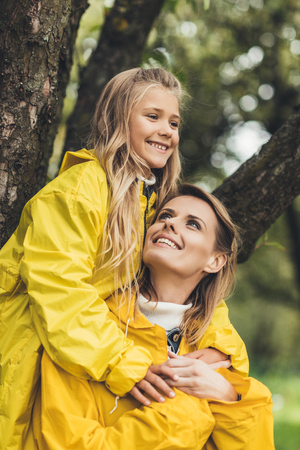 happy mother piggybacking her daughter in yellow raincoat  の写真素材