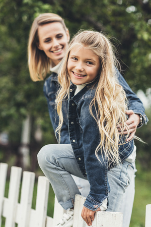 happy smiling mother and daughter on fence at countrysideの写真素材