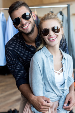 beautiful happy young couple in sunglasses smiling at camera in boutique の写真素材