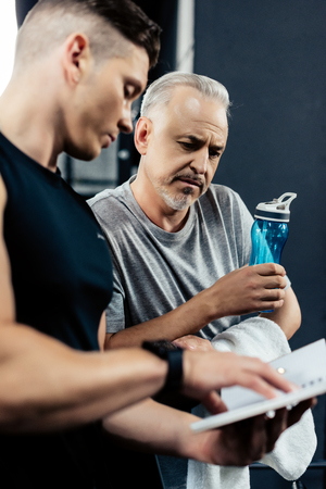 young trainer talking with senior sportsman in sport center