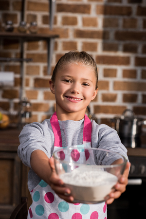 selective focus of little smiling girl holding bowl with ingredients in hands at homeの写真素材