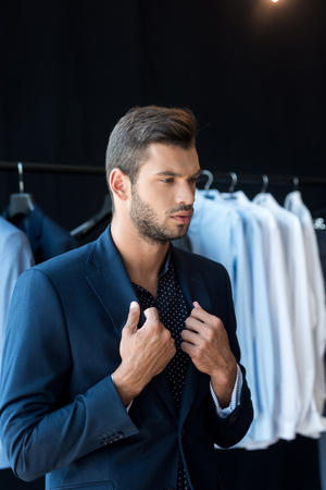 handsome young businessman trying on suit and looking away in boutique の写真素材
