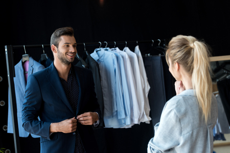 young couple looking at each other while man trying on suit in boutiqueの写真素材