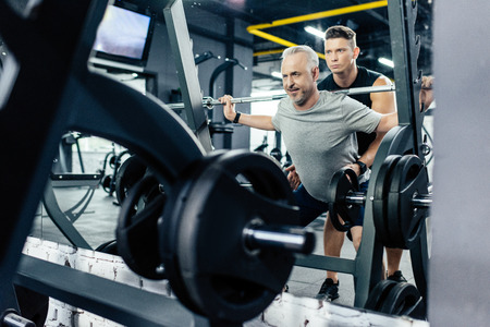 senior sportsman lifting barbell with trainer in gym   の写真素材