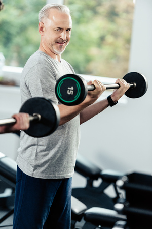 senior sportsman training with barbells and young trainer in gym    の写真素材