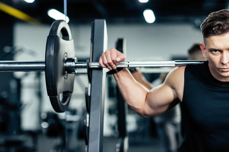 young muscular sportsman lifting barbell in sport centerの写真素材
