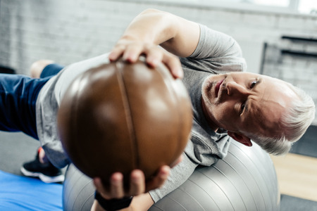 senior sportsman training on on fitness ball with medicine ball in gym  の写真素材