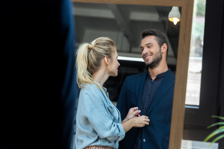 young couple smiling each other while choosing male suit in boutiqueの写真素材