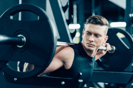 handsome young muscular sportsman lifting barbell in gymの写真素材