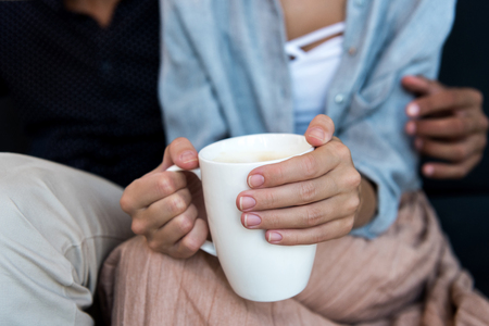 close-up partial view of young couple sitting together while woman holding cup of coffeeの写真素材