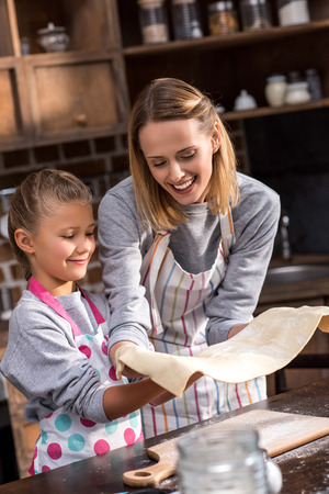 mother and preteen daughter in aprons making cookies together at homeの写真素材