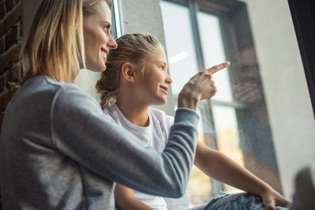 side view of mother and daughter looking out window together at homeの写真素材