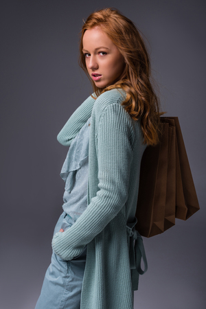attractive elegant redhead girl in blue clothes with shopping bags, isolated on grey の写真素材