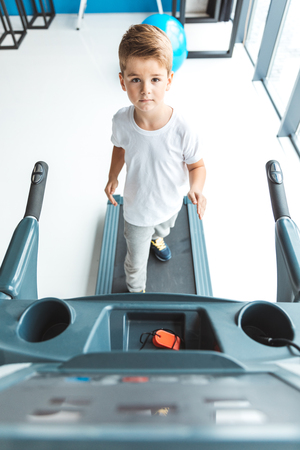 high angle view of cute little boy exercising on treadmill and looking at cameraの写真素材