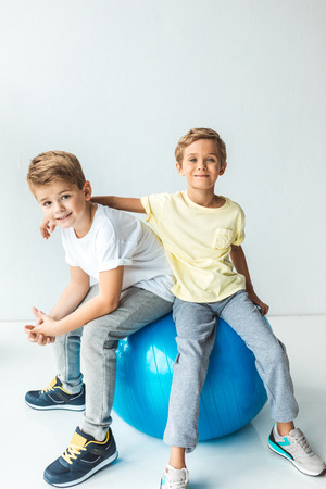 cute little boys sitting on fitness ball and smiling at camera on greyの写真素材