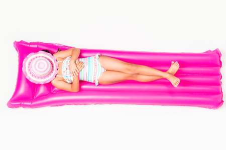 top view of cute little girl with hat on face resting on swimming mattress isolated on white