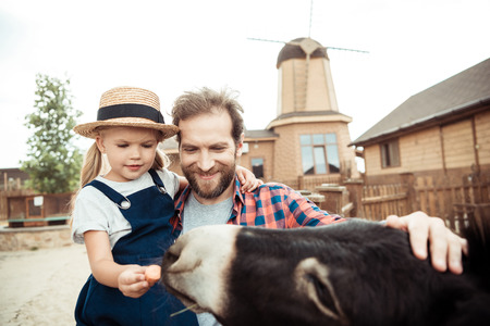 little girl and smiling father feeding donkey together in zooの写真素材
