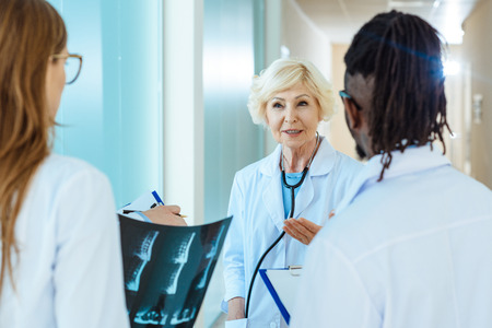Senior doctor in lab coat telling something to young medical interns holding x-ray photograph